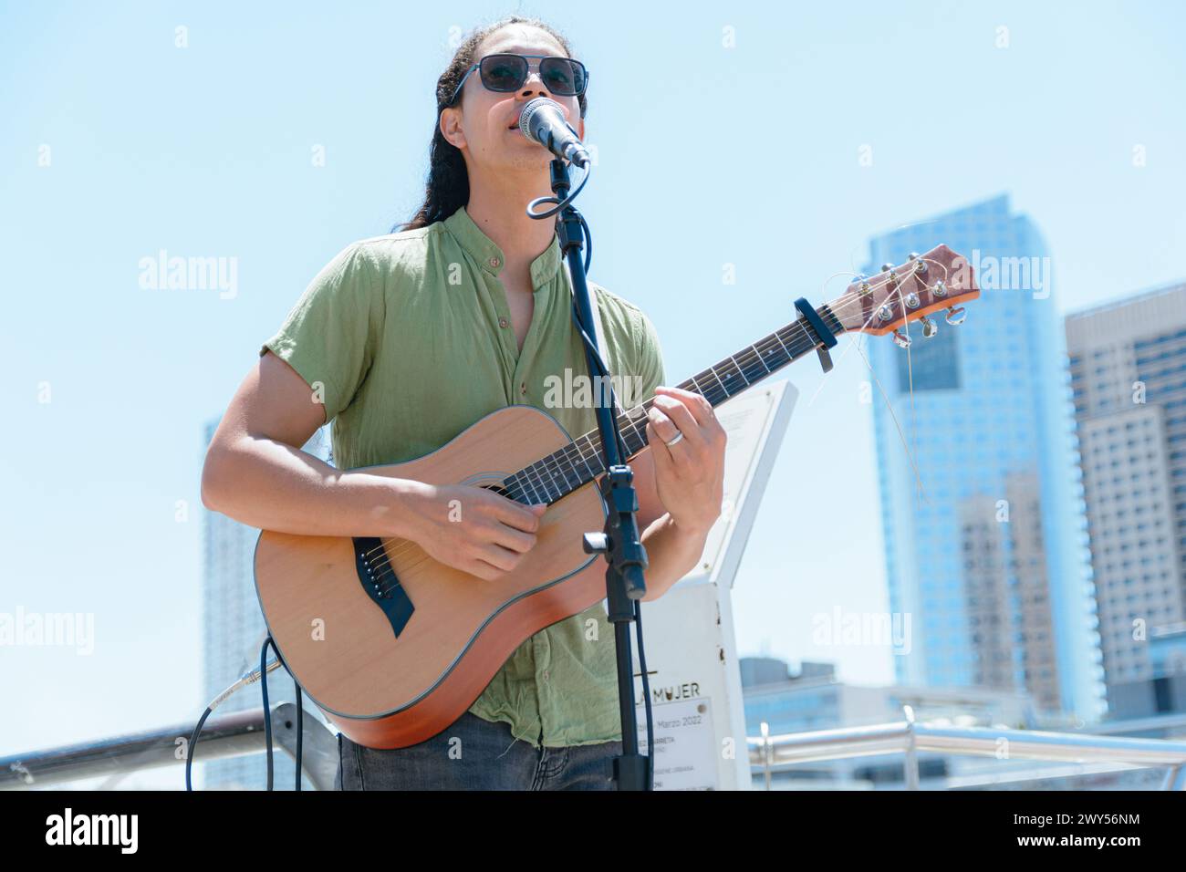 Jeune homme latin avec de longs cheveux et des lunettes de busker guitariste à Buenos Aires, travaillant à faire de l'art et de la musique de rue avec sa guitare, espace copie. Banque D'Images