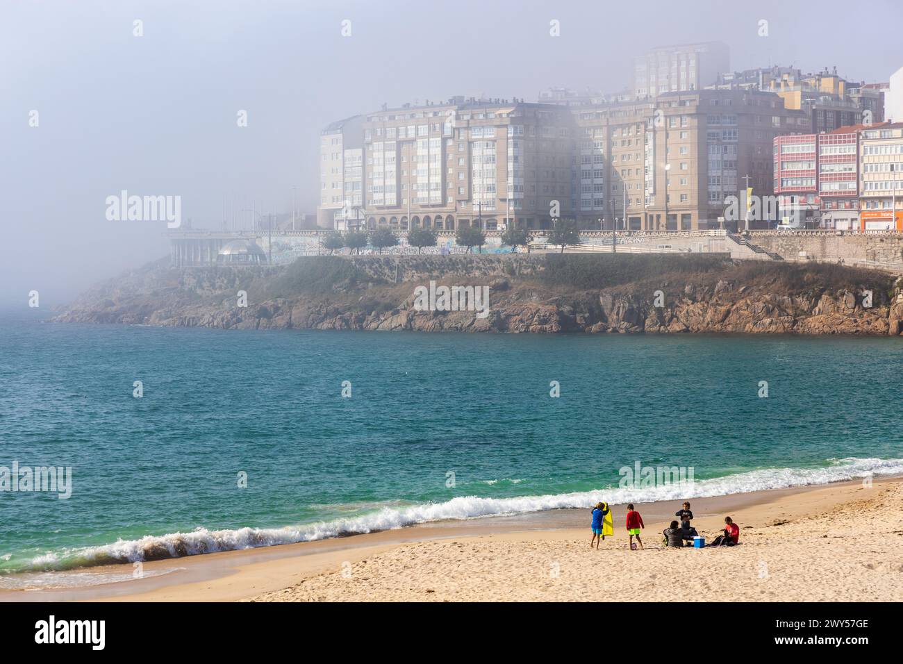 La plage de Orzán, l'océan Atlantique, le front de mer, et les bâtiments de la Coruña dans un épais brouillard. Journée ensoleillée. La Coruña, Galice, Espagne. Banque D'Images