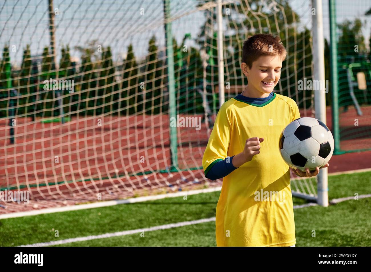 Un garçon talentueux portant un uniforme de football jaune vif tient un ballon de football en toute confiance, exsudant passion et détermination alors qu'il se prépare à un match. Banque D'Images