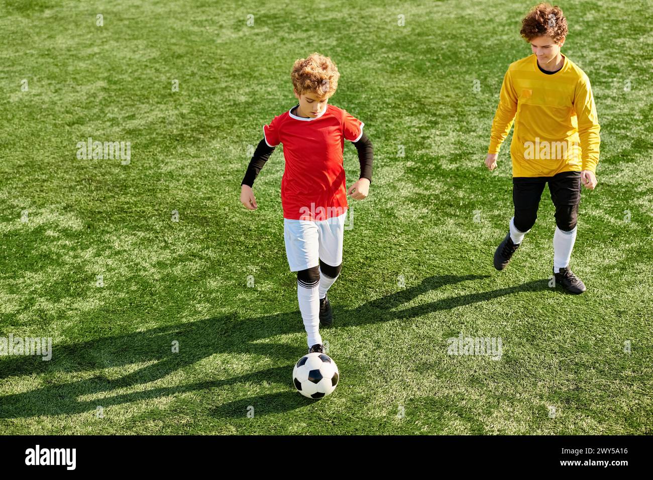 Deux jeunes hommes se sont engagés dans un jeu dynamique de football, courir, frapper et passer le ballon avec habileté et passion sur un terrain herbeux. Banque D'Images