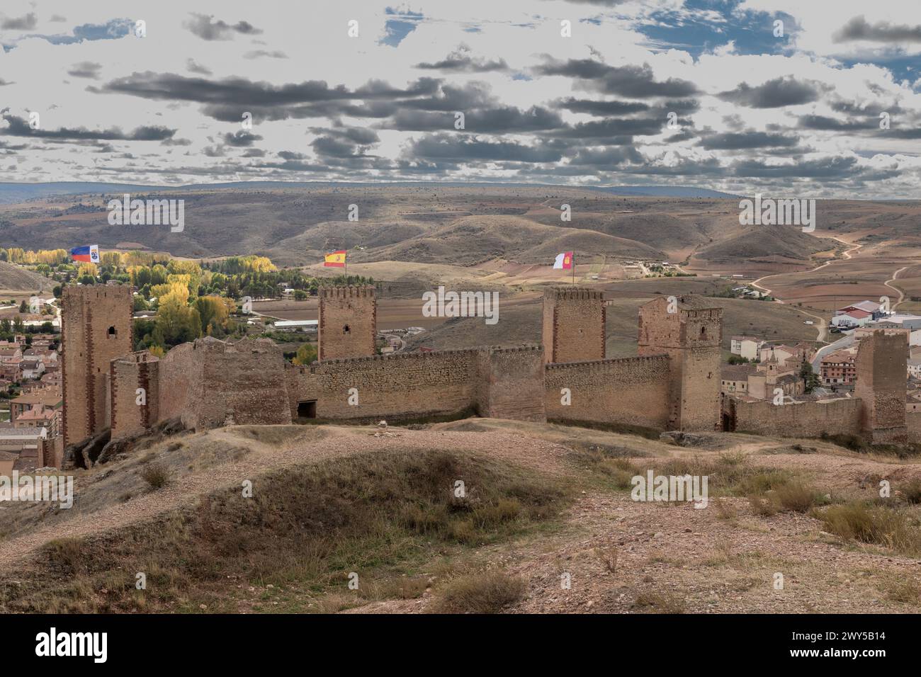 ancienne forteresse en pierre avec des drapeaux au sommet des tours surplombe une vallée sous un ciel lumineux et nuageux Banque D'Images