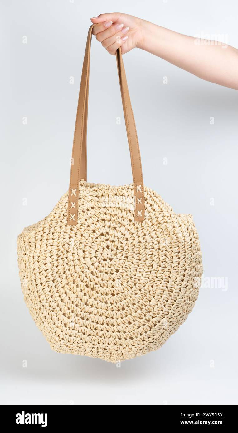 Sac à main marron de style plage d'été accroché sur la main de la femme isolé sur fond blanc de studio Banque D'Images