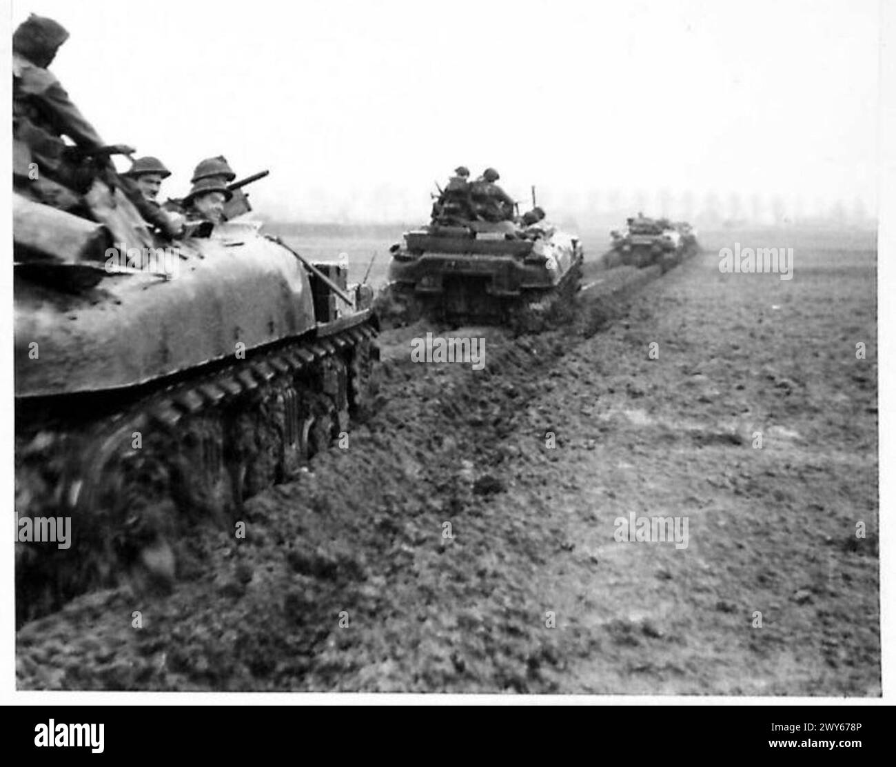 Les fantassins avancent sur des véhicules blindés de transport de troupes Kangourou dans des conditions boueuses vers Kervenhiem sous de fortes pluies, illustrant les opérations d'infanterie mécanisée sous l'armée britannique, 21e groupe d'armées. Banque D'Images