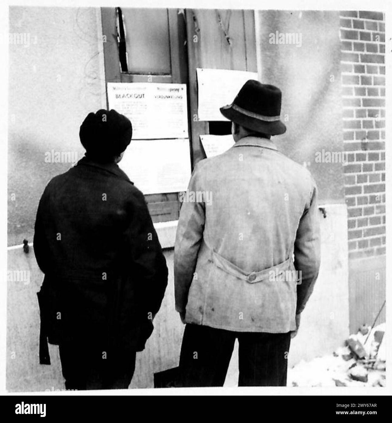 L'ALLEMAGNE PAIE LE PRIX DANS le 'TRIANGLE SITTARD' - deux garçons allemands lisant l'ordre de couvre-feu devant la maison du bourgmestre. , Armée britannique, 21e groupe d'armées Banque D'Images