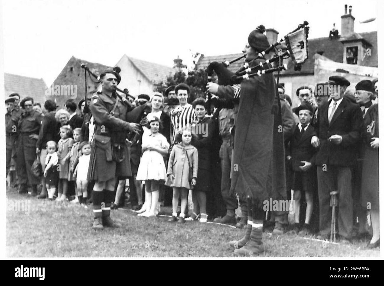 Des civils français observent des cornemuses se produisant avant un match de football le jour de la Bastille pendant la présence de l'armée britannique, du 21e groupe d'armées. Banque D'Images