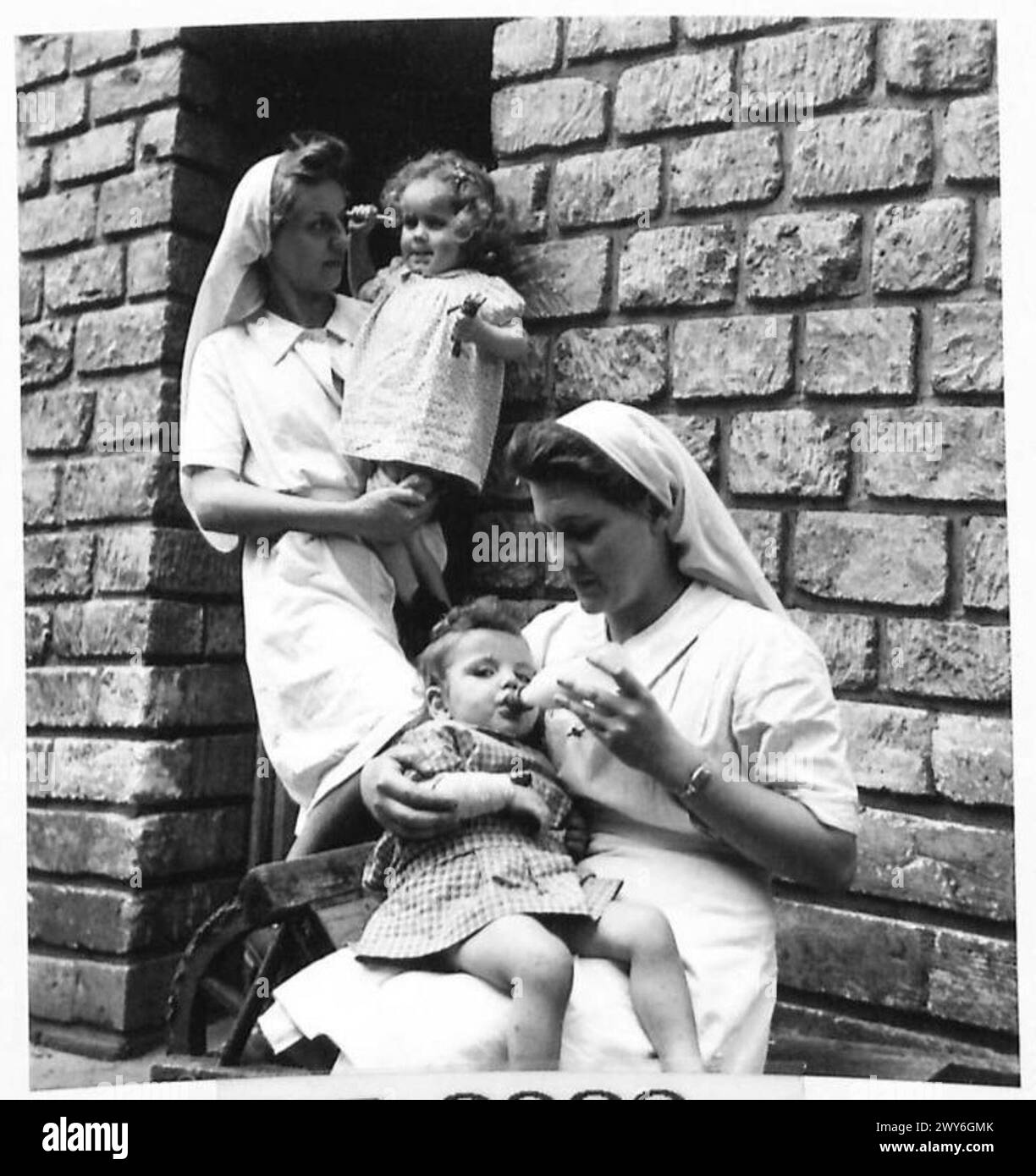 Les orphelins Josette et Henriette sont nourris près d'une entrée de cave à la maternité de Benouville, permettant un abri rapide pendant les bombardements potentiels, sous la supervision de l'armée britannique. Banque D'Images