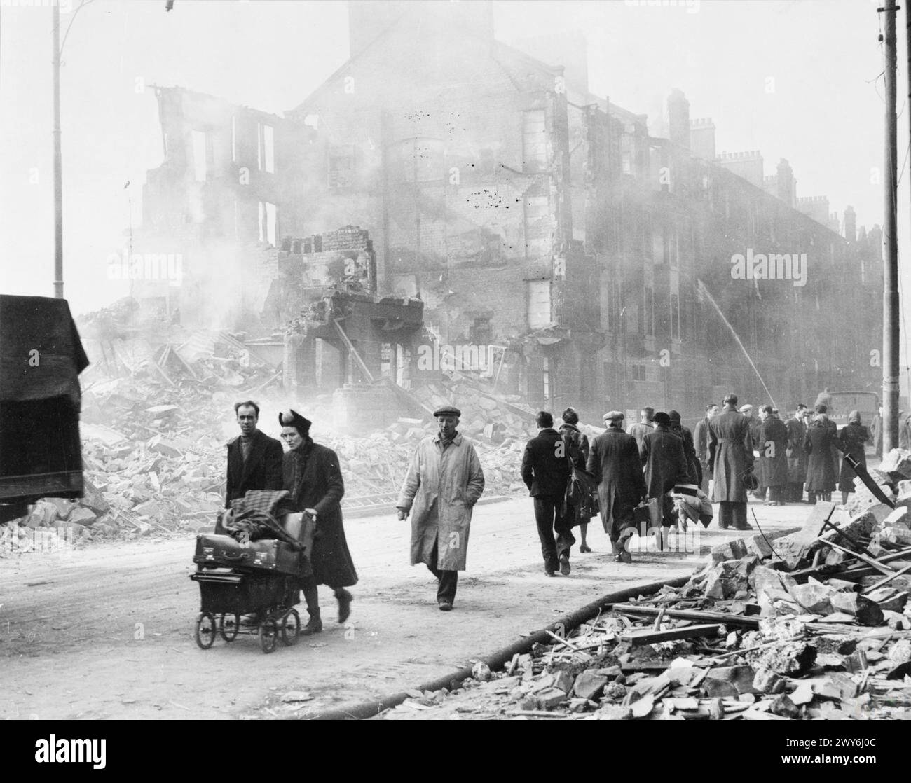 Des gens sont montrés marchant devant des maisons d'habitation bombardées à Glasgow lors de raids aériens de la seconde Guerre mondiale, portant des biens récupérés. Banque D'Images