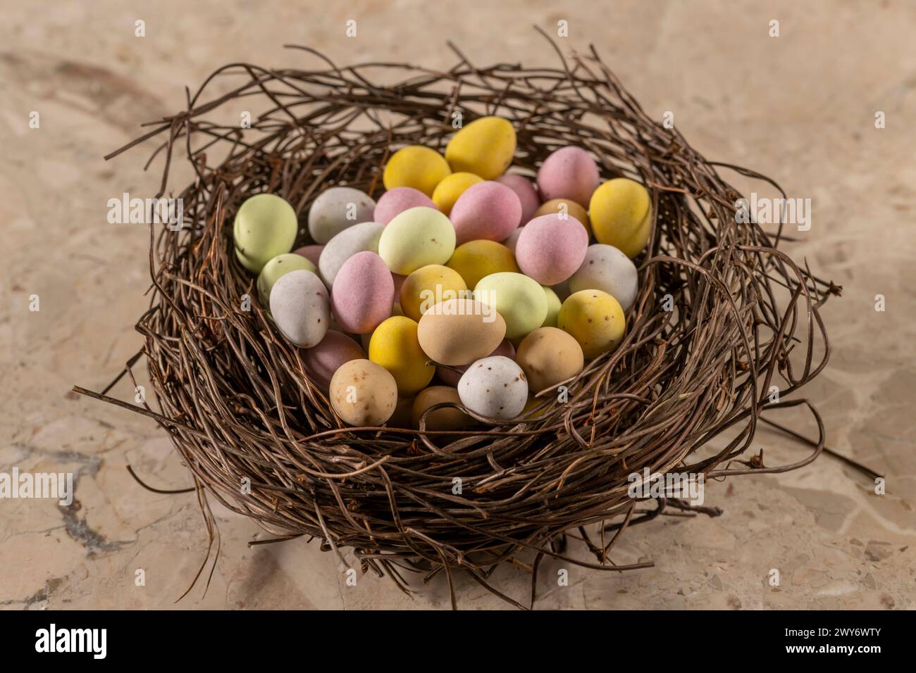Mini oeufs colorés enrobés de sucre disposés dans un faux nid d'oiseau. Banque D'Images