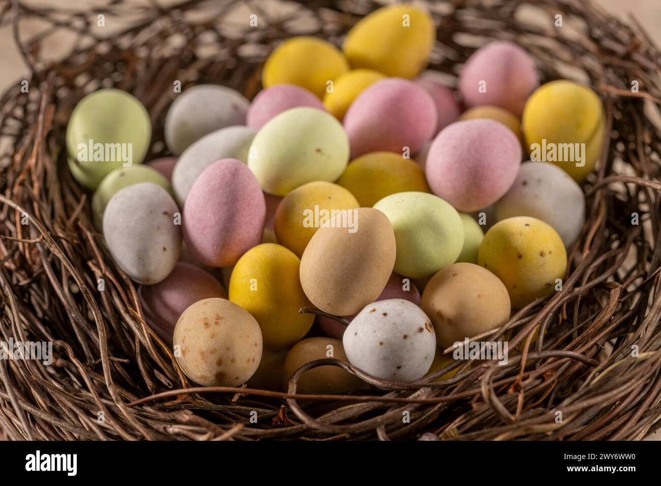 Gros plan de mini-œufs en chocolat enrobés de sucre colorés disposés dans un faux nid d'oiseau. Banque D'Images