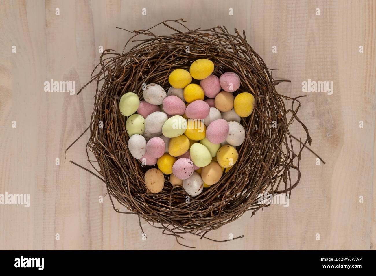 Vue en plan de mini-œufs enrobés de sucre colorés disposés dans un faux nid d'oiseau. Banque D'Images