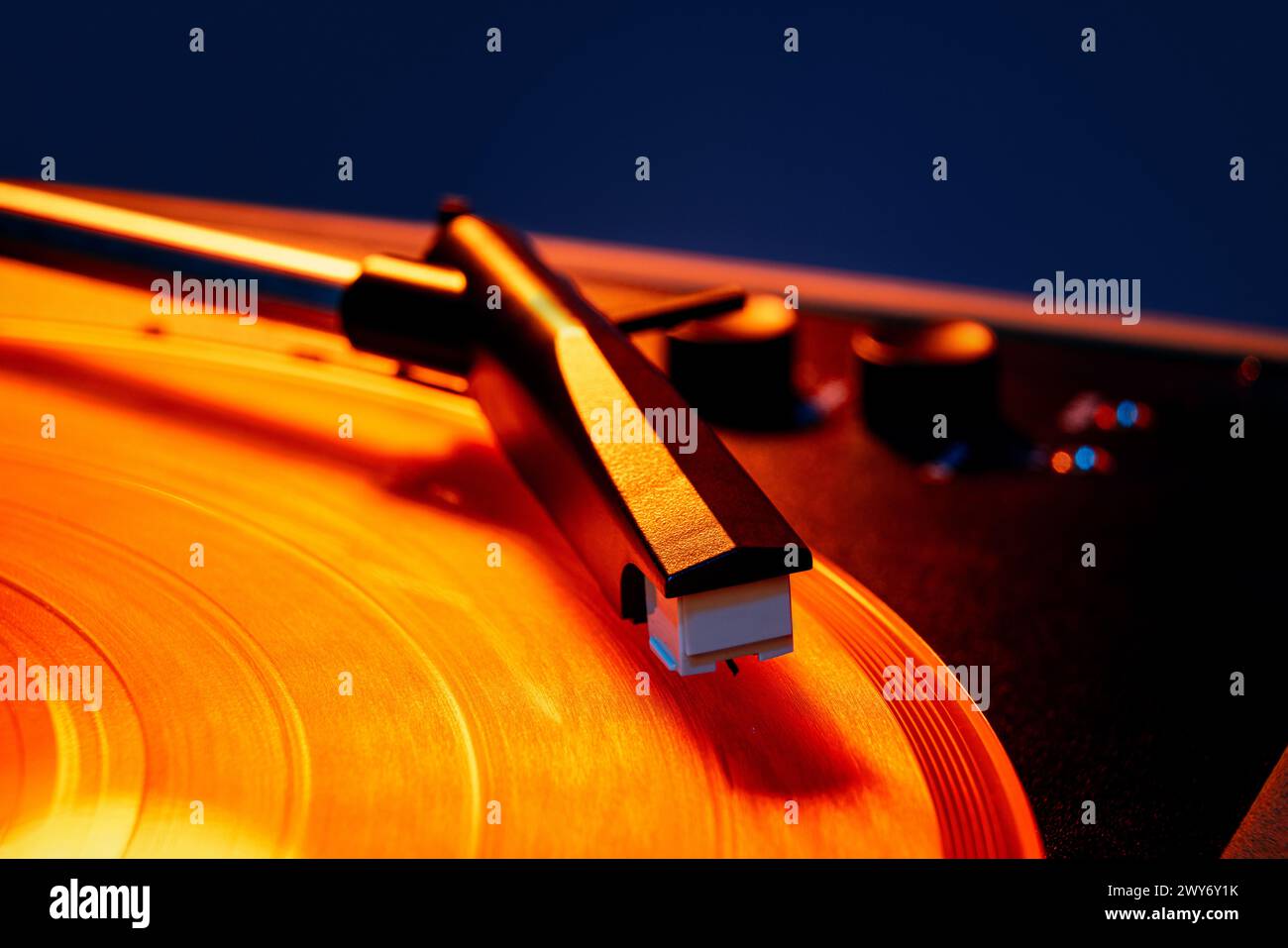 Macro photo de lecteur de vinyle rétro, aiguille phonographe chevauchant des vagues de la surface du vinyle dans une lumière orange chaude. Disco. Banque D'Images