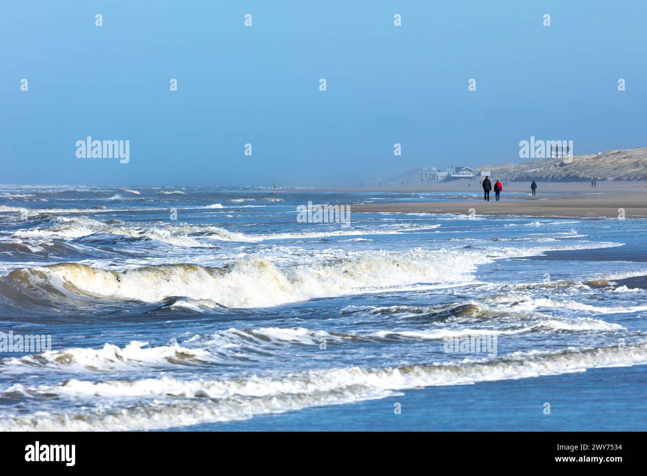 Egmond aan Zee, pays-Bas - 17 mars 2022 : vagues dans la mer du Nord agitée avec quelques personnes marchant le long du rivage au soleil Banque D'Images