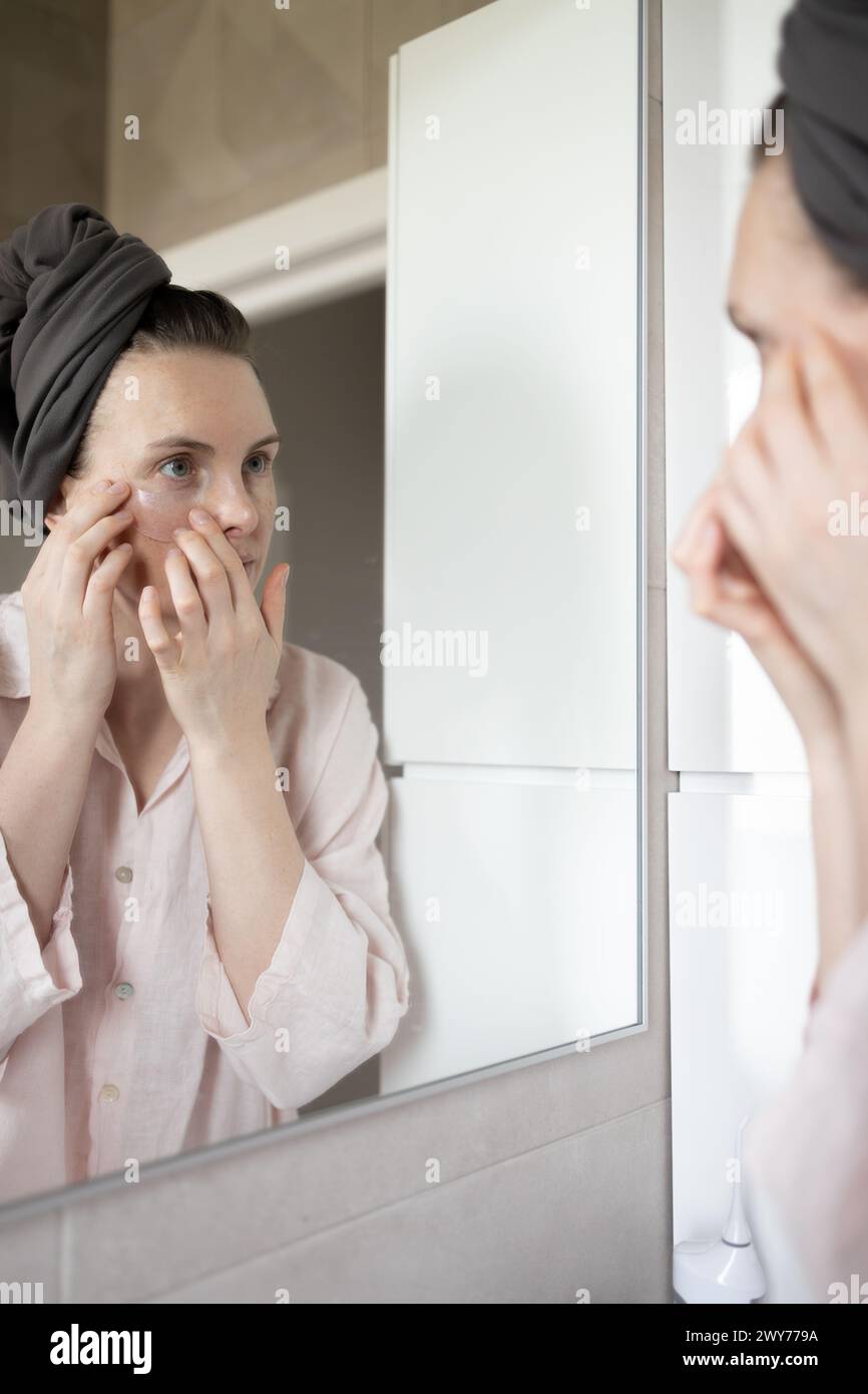 Femme appliquant des patchs oculaires dans la salle de bain Banque D'Images