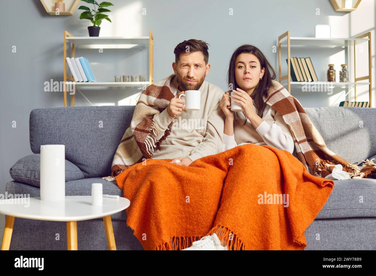 L'homme et la femme sont à la maison dans le salon, enveloppés dans une couverture chaude et ressentent les symptômes de la grippe. Banque D'Images
