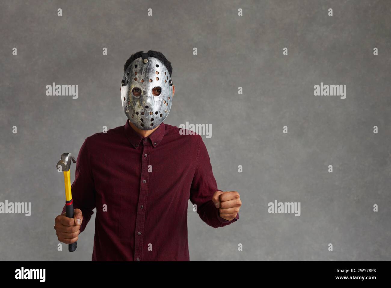 Homme noir dans le masque effrayant tenant le marteau debout isolé sur fond gris d'espace de copie Banque D'Images