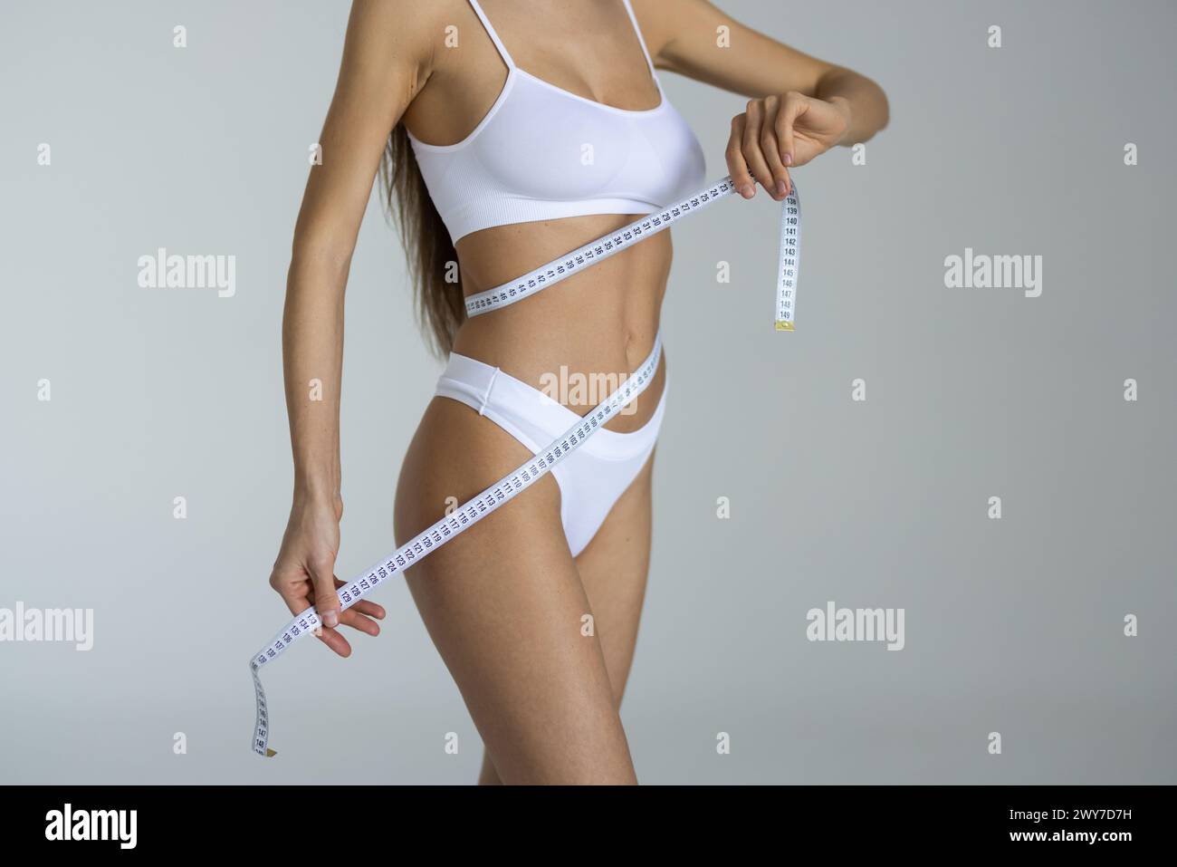 La taille minuscule est intemporelle. Photo studio d'une femme méconnaissable mesurant sa taille sur un fond blanc. Banque D'Images