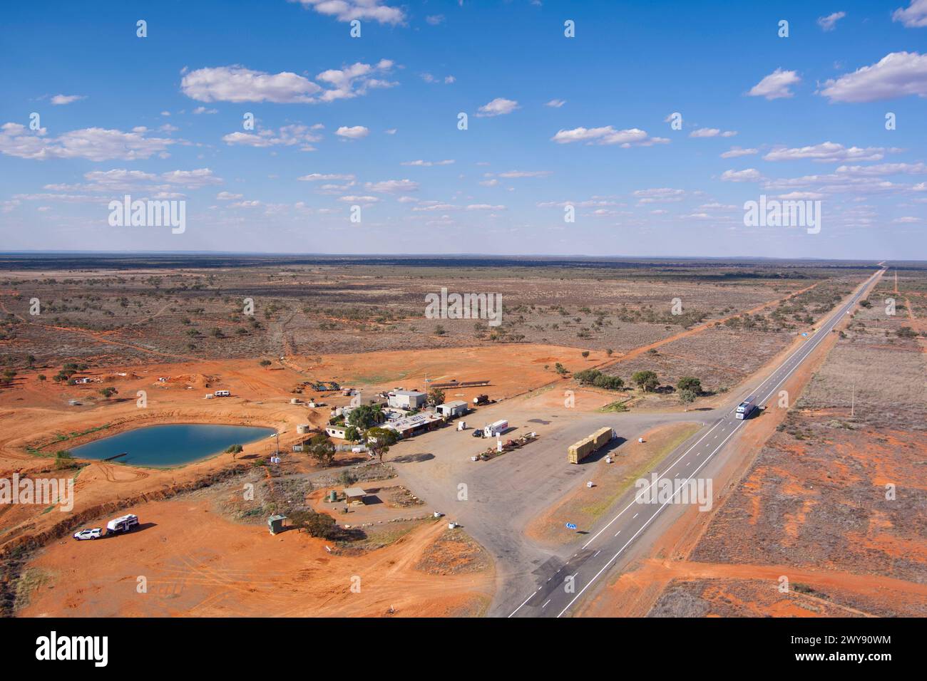 Vue aérienne d'une station-service éloignée avec une route s'étendant à travers un paysage aride sous le ciel bleu Banque D'Images