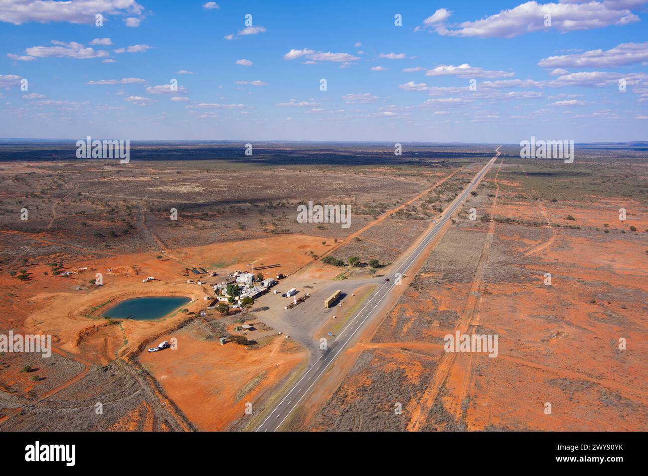 Vue aérienne d'une autoroute voyageant à travers un paysage aride avec une petite colonie de bord de route et un ciel bleu clair Banque D'Images