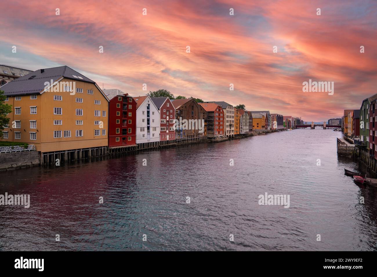 Des maisons sur pilotis colorées bordent la rivière Nidelva dans le quartier de Trondheim Brygge sous un ciel de coucher de soleil vibrant en soirée. Destination touristique Norvège Banque D'Images