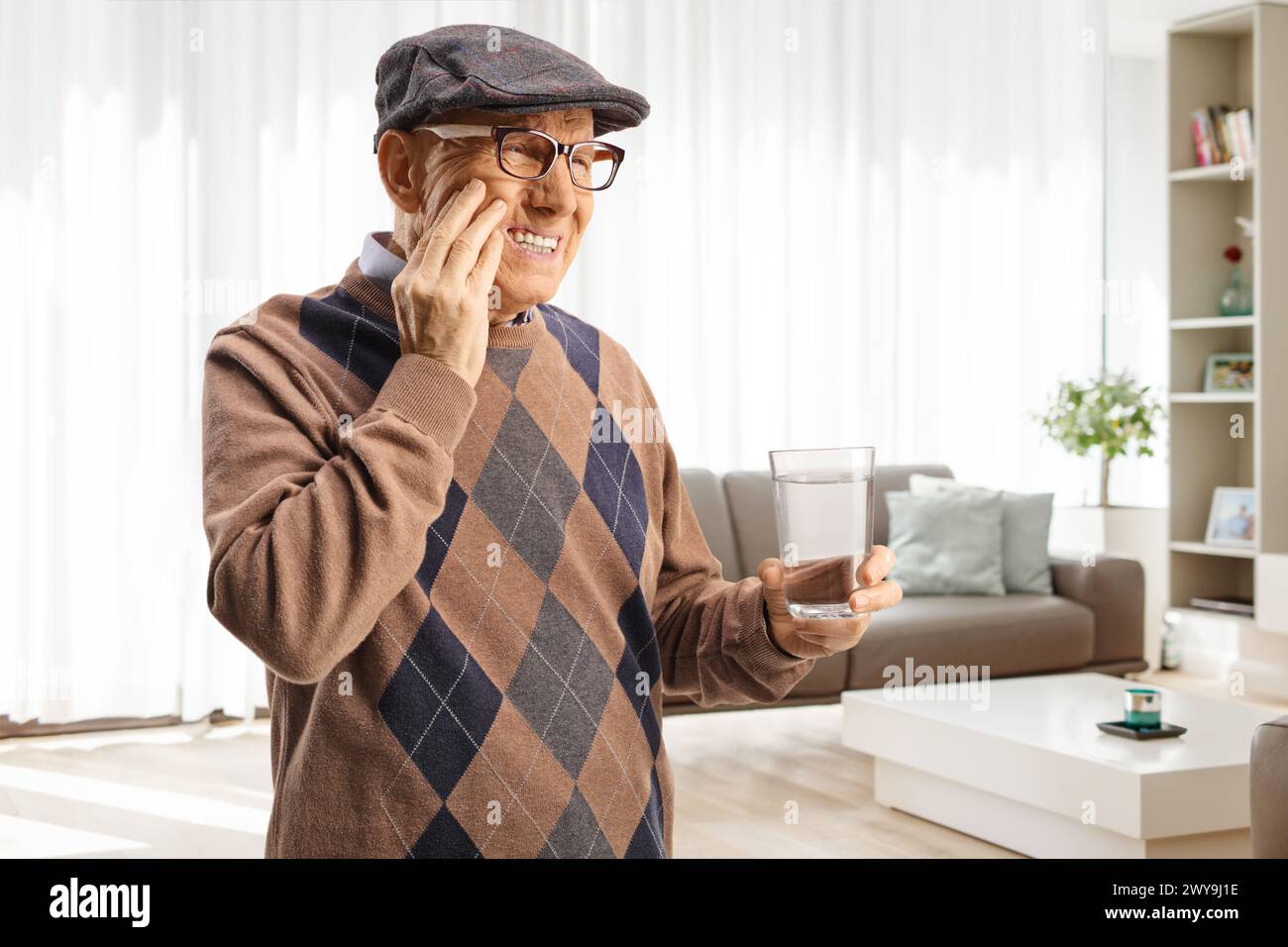 Homme âgé avec un mal de dents tenant un verre d'eau à la maison dans un salon Banque D'Images