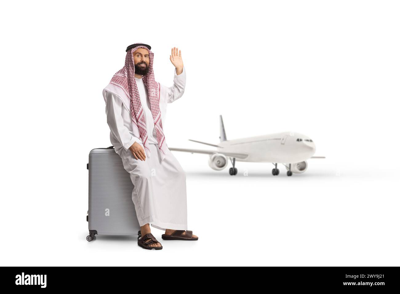 Homme arabe saoudien assis sur une valise près d'un avion et agitant isolé sur fond blanc Banque D'Images