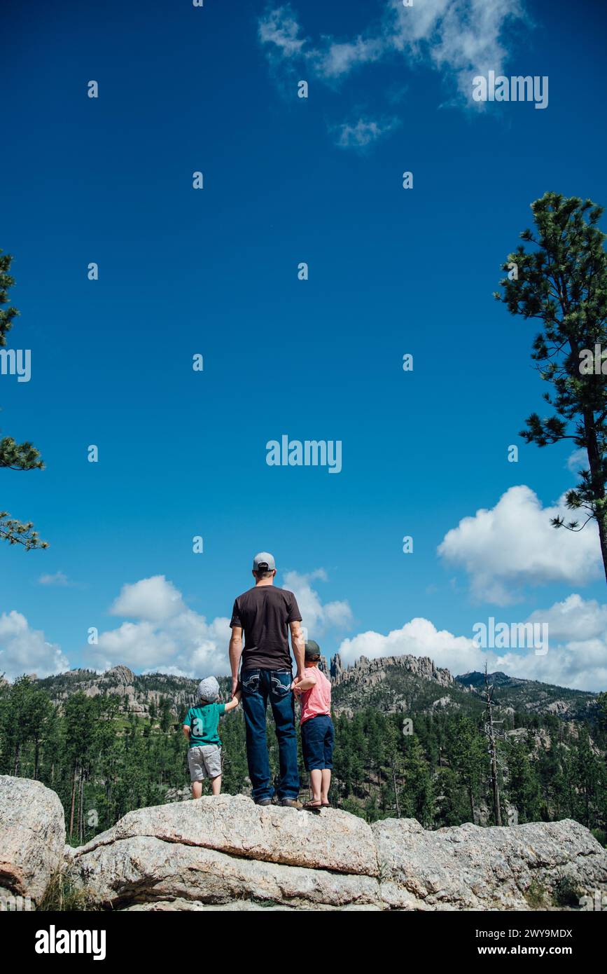 Papa et ses deux fils se tiennent debout sur des rochers surplombant les montagnes et le ciel Banque D'Images