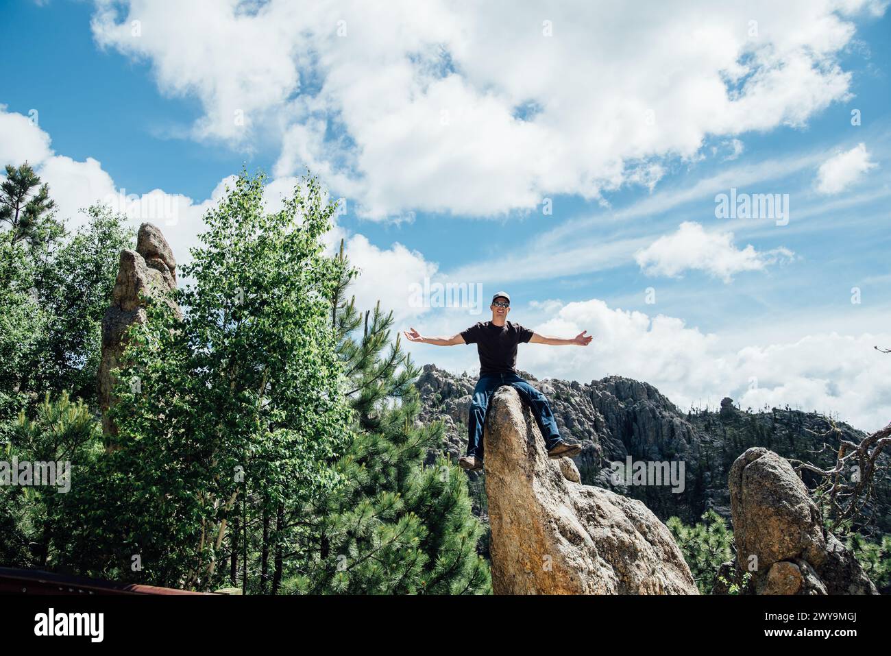 Homme avec les bras tendus assis sur les rochers dans la scène ensoleillée de montagne Banque D'Images
