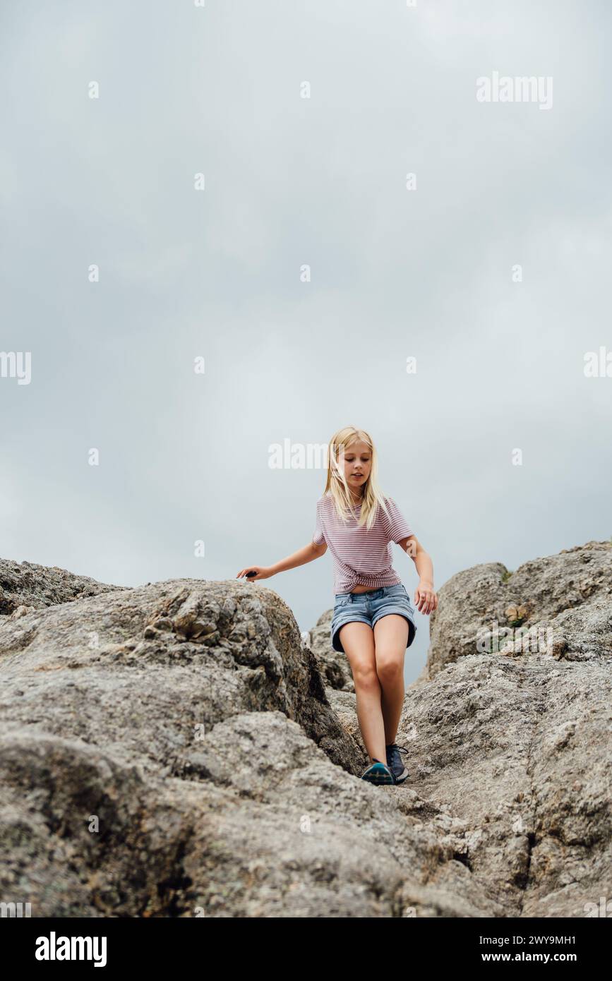 Vue basse d'une jeune fille de preteen descendant les rochers contre le ciel nuageux. Banque D'Images