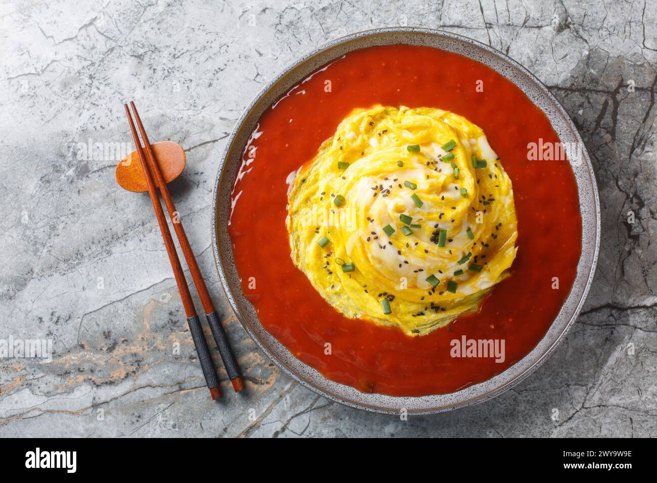 Tornade omelette tourbillonnante asiatique avec riz frit et sauce piquante gros plan dans une assiette sur la table. Vue horizontale de dessus Banque D'Images