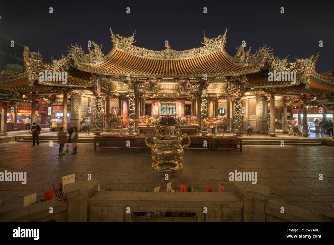 La photo montre une porte d'entrée du temple Longshan richement décorée avec des sculptures complexes et animée de fidèles la nuit Banque D'Images