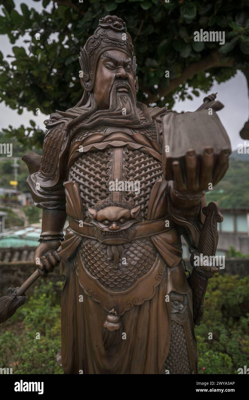 Statue en bronze minutieusement détaillée d'un guerrier chinois traditionnel en armure historique, debout sous un arbre Banque D'Images