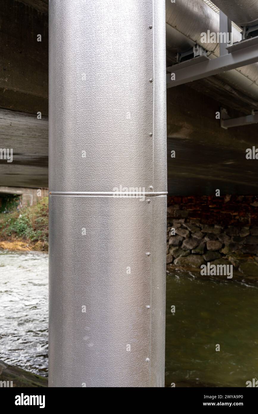 Conduites de chauffage urbain sous et à côté d'un pont sur une rivière. Banque D'Images