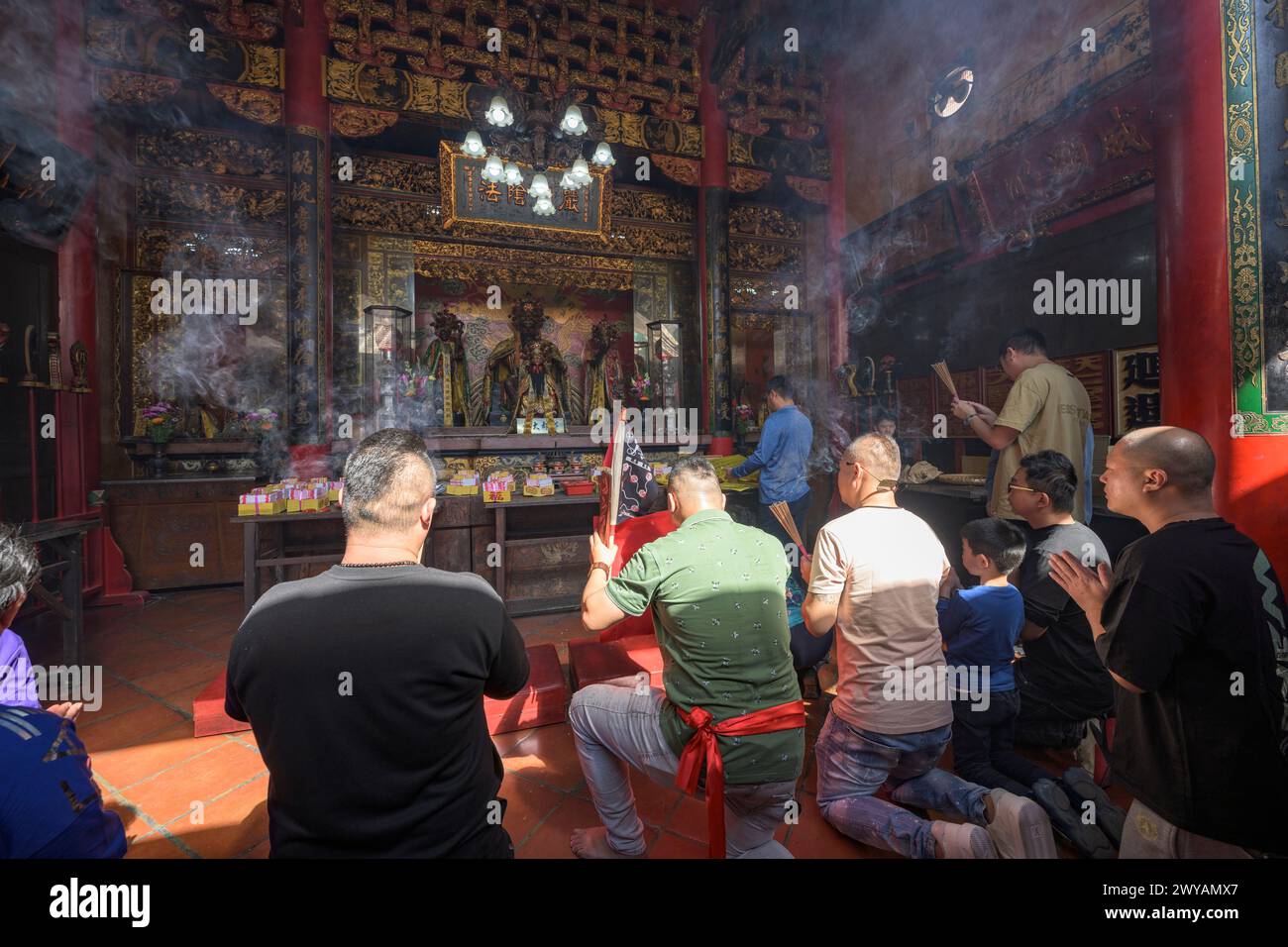 Les adorateurs allument de l'encens et prient dans l'intérieur fumé d'un temple traditionnel Banque D'Images