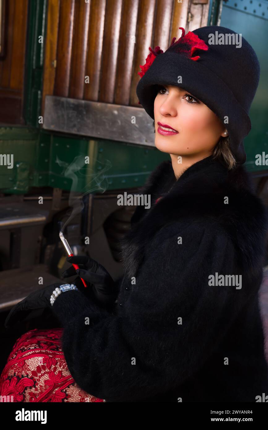 Belle jeune femme en robe rouge 1920s flapper et chapeau de manteau voyageant en train antique de vapeur Banque D'Images