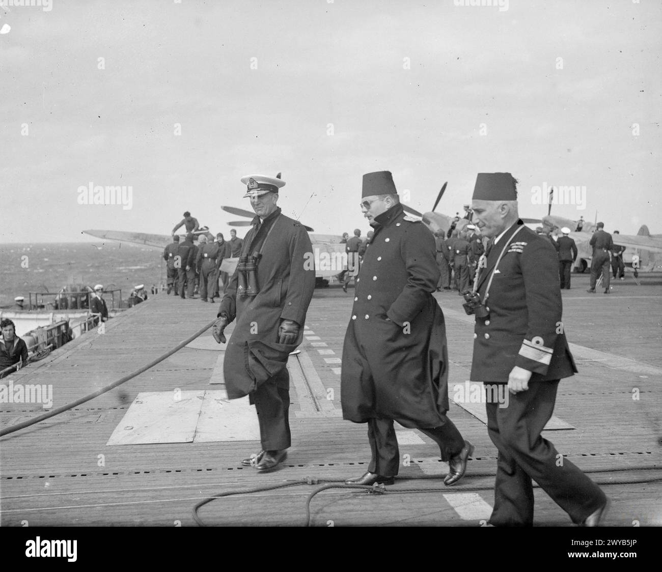 LE ROI FAROUK VISITE LE PORTE-AVIONS D'ESCORTE BRITANNIQUE. MARS 1945, À BORD DU HMS HUNTER, ALEXANDRIE, ÉGYPTE. - Le roi Farouk traverse le pont d'envol avec l'amiral Tennant, sur la droite se trouve le contre-amiral Salem Pash El Badan. , Banque D'Images