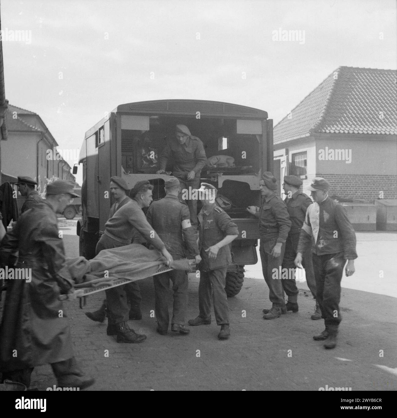 Les prisonniers de guerre allemands et les agents du corps médical de la Royal Army britannique en vêtements de protection déchargent les prisonniers malades des ambulances de la station de nettoyage de Bergen-Belsen gérée par le laboratoire de bactériologie mobile n° 7 dans le camp n° 2, Hohne Barracks. Banque D'Images