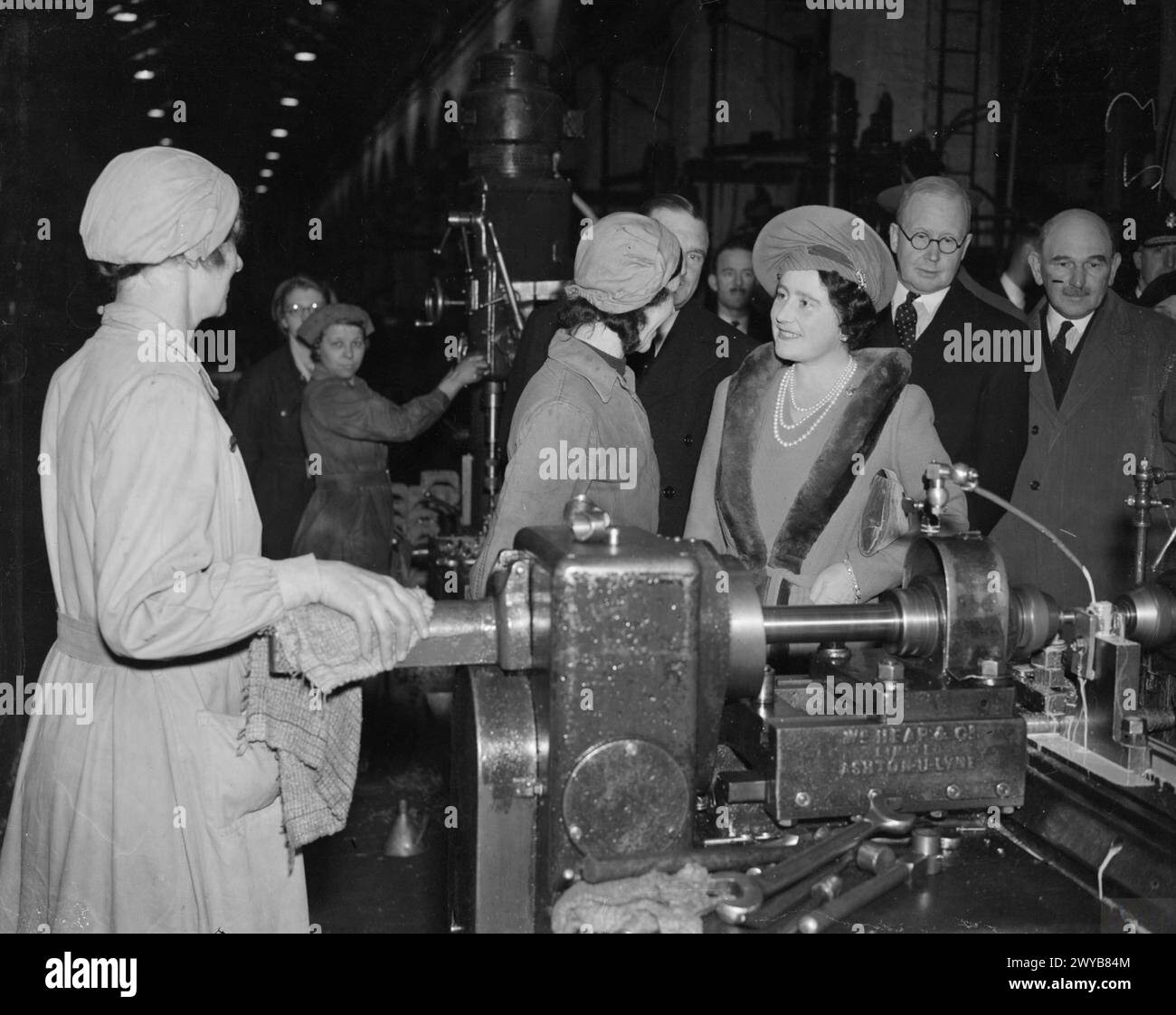 UNE VISITE ROYALE À THORP ARCH ROYAL ORDNANCE FACTORY, WETHERBY, YORKSHIRE, ANGLETERRE, ROYAUME-UNI, 1941 - sa Majesté la Reine Elizabeth parle aux travailleurs des munitions à leurs machines lors d'une visite à ROF Thorp Arch. , Elizabeth, Reine Banque D'Images