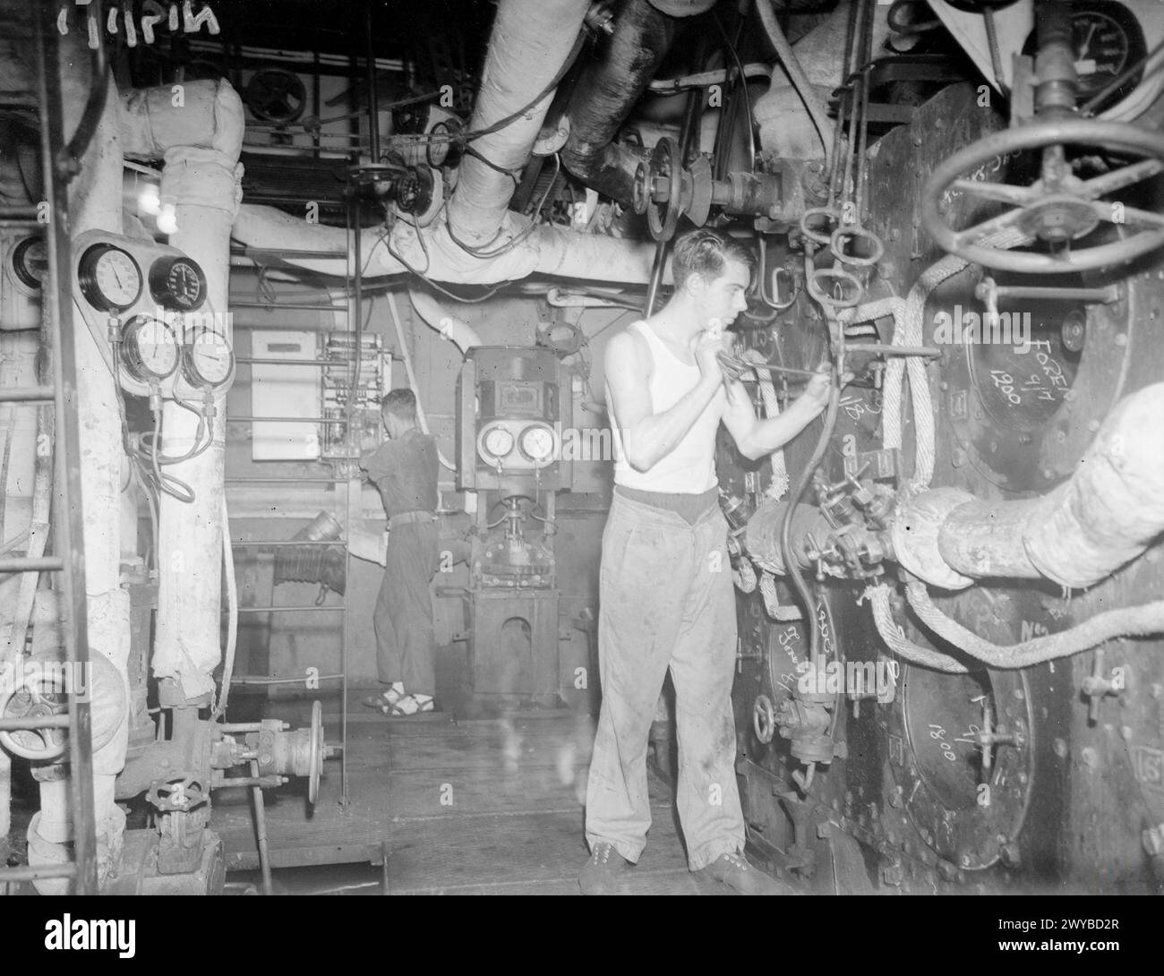 LA MODERNE « ÉQUIPE NOIRE ». LE 9 AOÛT 1945, À BORD DU CROISEUR HMS NIGERIA, DU DESTROYER HMS TARTAR ET DE L'UN DES DRAGUEURS DE MINES HM. LE TRAVAIL DES STOKERS DE LA NAVY DANS LES TROPIQUES SERVANT AVEC LA FLOTTE DES INDES ORIENTALES BRITANNIQUES. - Le «crime» que le stoker dans la chaufferie ne doit pas commettre est de «faire de la fumée», ce qui peut donner la position du navire à l'ennemi. Les pulvérisateurs sales, obstrués par de l'huile/carburant coagulé peuvent provoquer une « fumée noire ». Il en va de même pour les « glaçons » de carbone qui se forment autour du cône. Ici, à bord du NIGERIA Stoker P Higgins de Sittingbourne, Kent, détruit certaines des fondations en carbone croûtées wi Banque D'Images