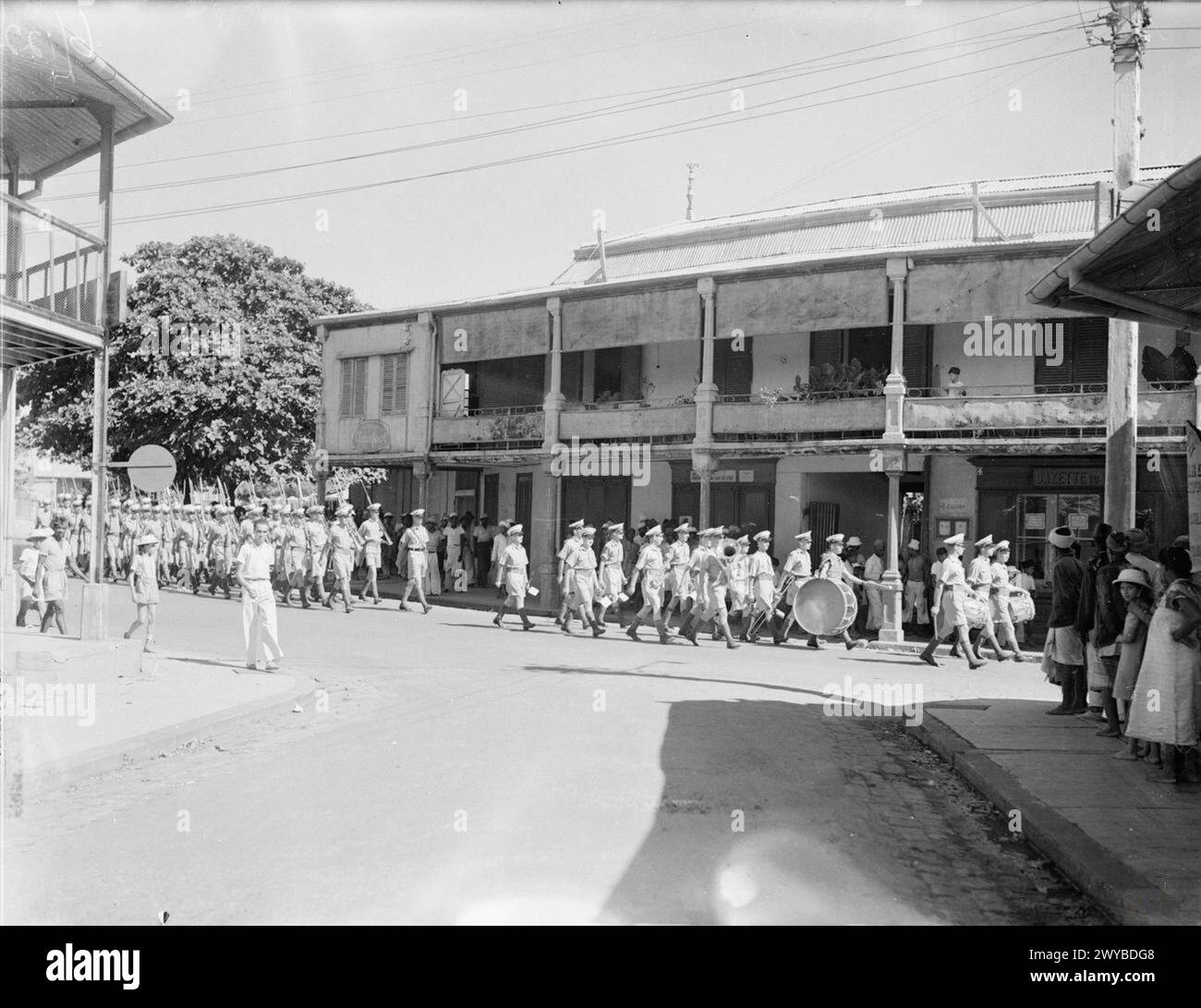 LES OPÉRATIONS BRITANNIQUES À MADAGASCAR. 8 MAI 1942, À BORD DU CUIRASSÉ HMS RAMILLIES ET SUR MADAGASCAR. LES OPÉRATIONS MARITIMES, AÉRIENNES ET TERRESTRES BRITANNIQUES À MADAGASCAR ONT ÉTÉ COURTES, PRÉCISES ET RÉUSSIES. LES FORCES FRANÇAISES SE RENDIRENT ET UN PROTOCOLE DE PAIX FUT SIGNÉ À ANTSIRANE PAR LEQUEL LES BRITANNIQUES PRIRENT POSSESSION DE LA BASE NAVALE DE DIEGO SUAREZ. - Royal Marines marchant dans les rues d'Antsirane après la conférence du traité de reddition. , Banque D'Images