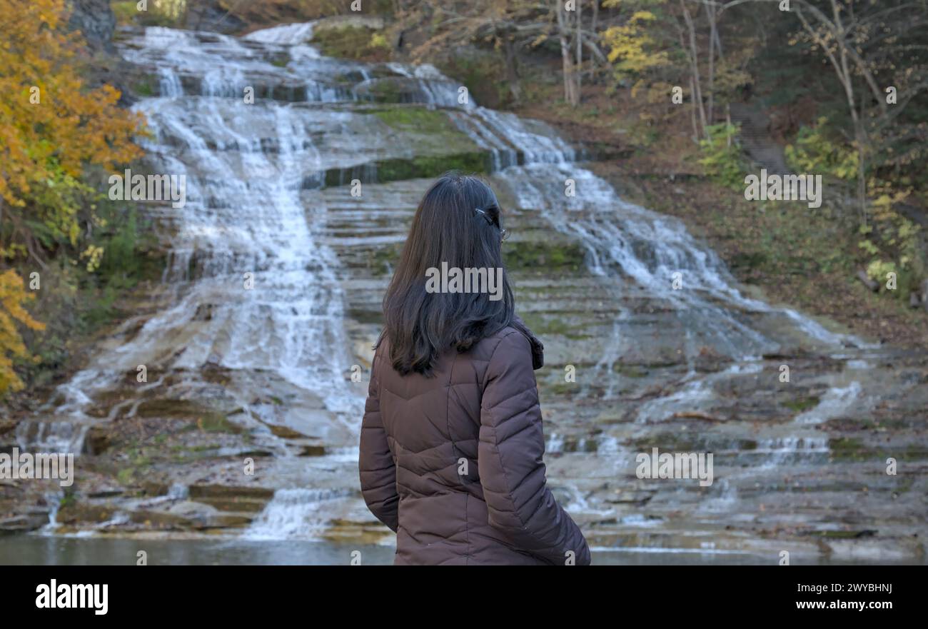 femme regardant une cascade sur une randonnée dans la nature (photographiée de derrière) portant chapeau d'hiver, veste brune (buttermilk falls parc d'état à ithaca new y Banque D'Images