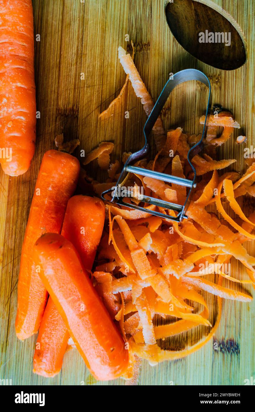 Carottes biologiques hachées et pelées avec un éplucheur sur une planche à découper en bois Banque D'Images