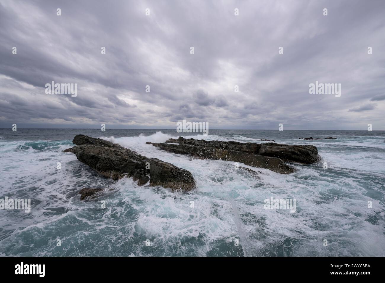 Des formations rocheuses captivantes sur fond de puissantes vagues à sommet blanc sous un ciel orageux Banque D'Images