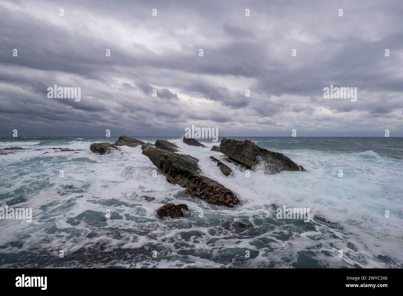Des formations rocheuses captivantes sur fond de puissantes vagues à sommet blanc sous un ciel orageux Banque D'Images