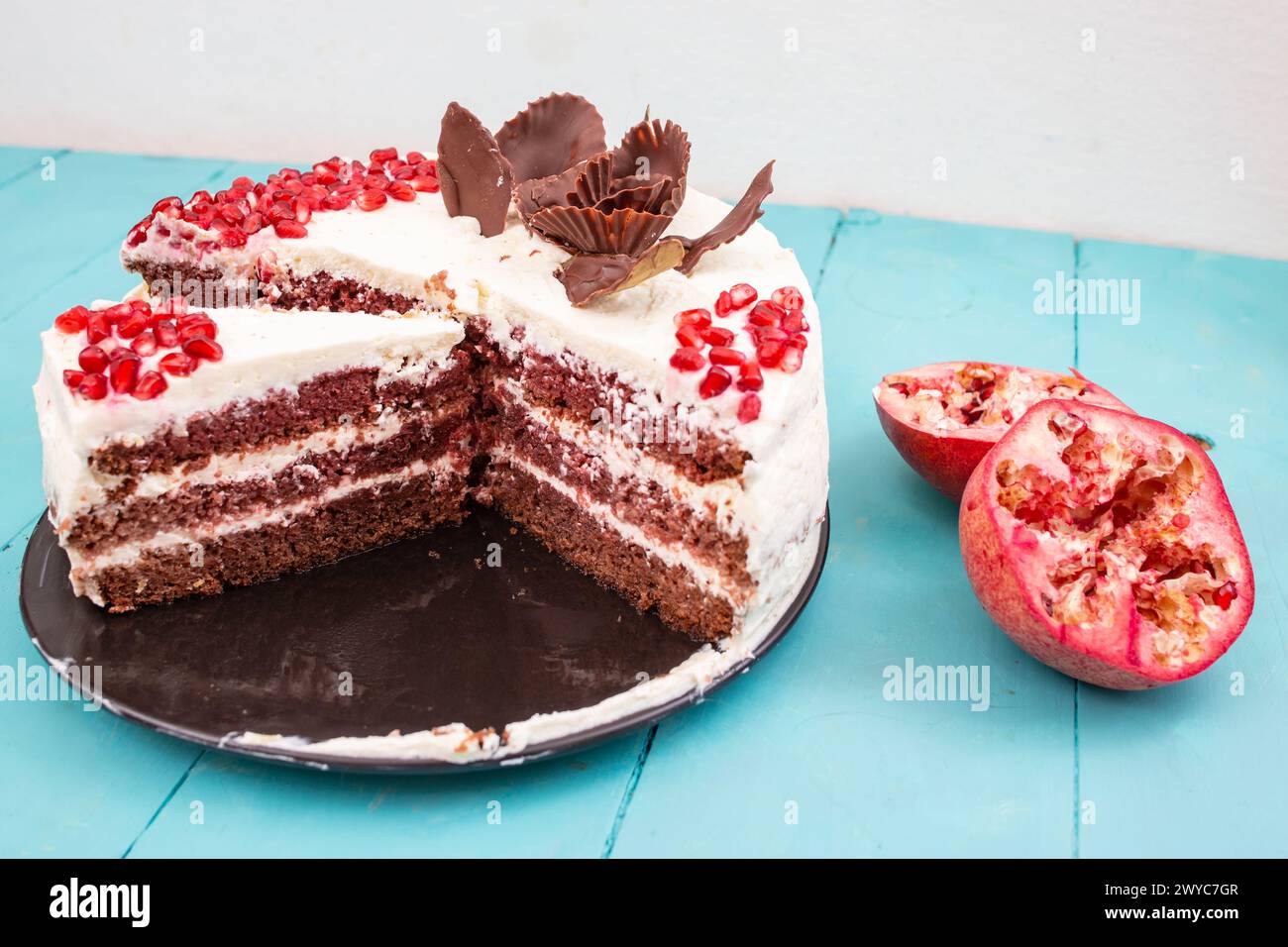 Gâteau de velours rouge aux graines de grenade, tranché sur une plaque de céramique noire, sur une table, soft focus gros plan Banque D'Images