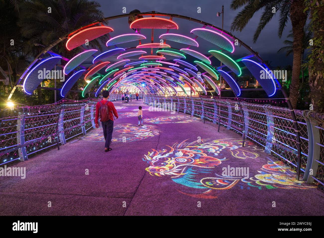 Les gens marchent sous une arche illuminée colorée avec des projections de 2024 ans et des caractères chinois la nuit Banque D'Images
