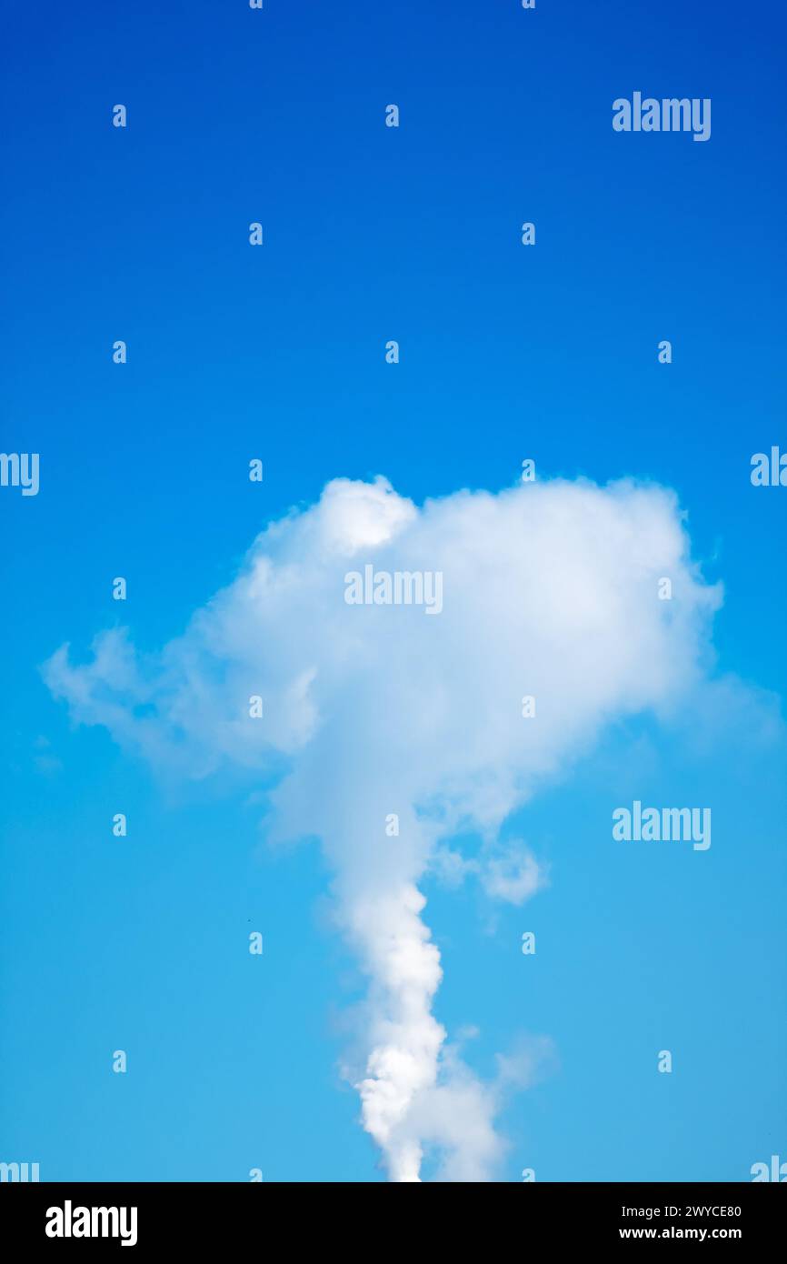 Un nuage de fumée monte dans le ciel au-dessus d'un ciel bleu clair. La fumée est blanche et bouillonnante, créant une sensation de mouvement et d'énergie. Le contraste Banque D'Images