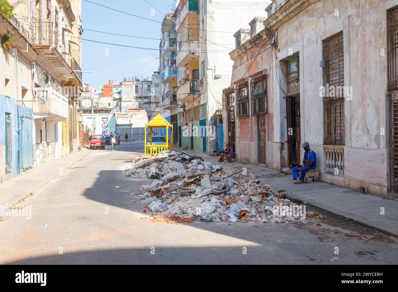 Homme cubain assis sur le trottoir, tas de gravats dans la rue de la ville à la Havane, Cuba Banque D'Images