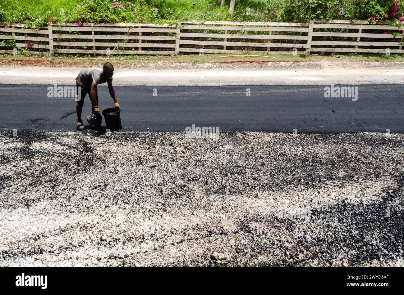 Un homme sur une route est sur le point de verser de l'huile noire d'un seau noir à un contaier plus petit. Banque D'Images