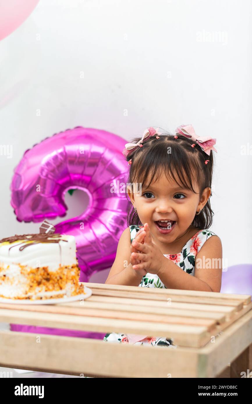 petite fille brune latine très heureuse et souriante tout en applaudissant pour son anniversaire, petit gâteau Banque D'Images