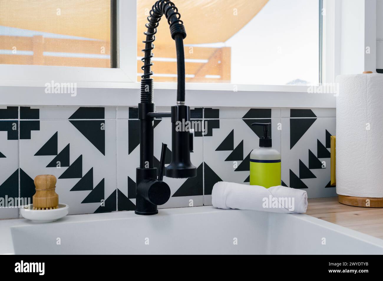 Évier de robinet et distributeur de savon à une fenêtre de cuisine dans une cuisine moderne avec des carreaux noirs et blancs Banque D'Images